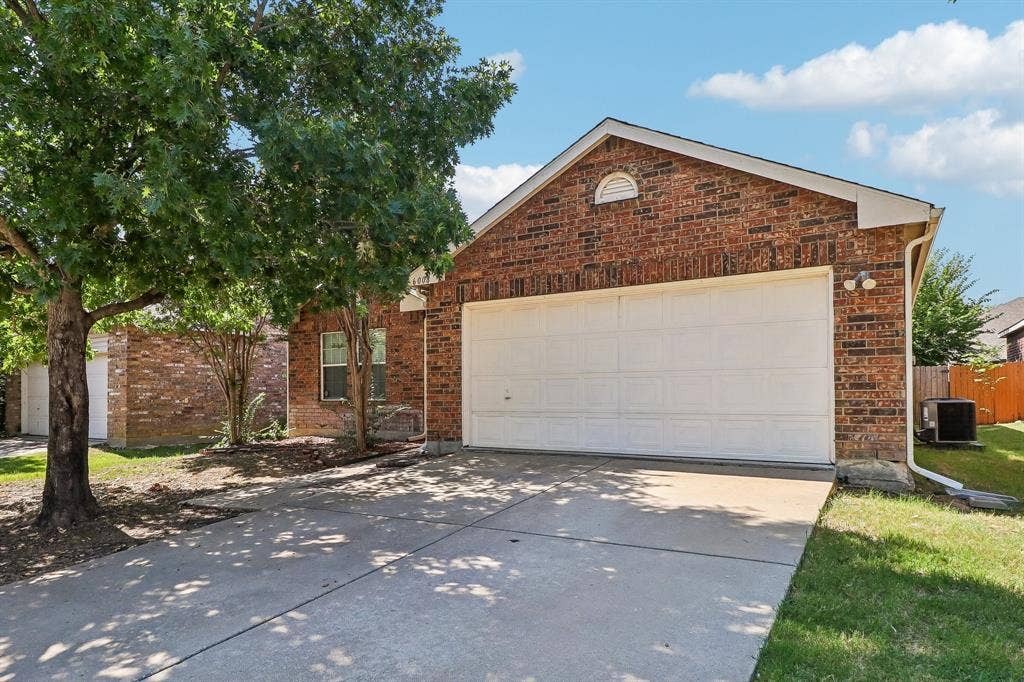 Brick facade residence featuring an attached garage with a concrete driveway, mature trees, and a manicured lawn