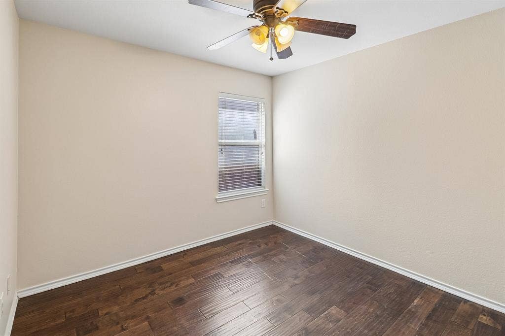 Room featuring wood-finish flooring, light-toned walls, a single window with blinds, and a ceiling fan with integrated lighting