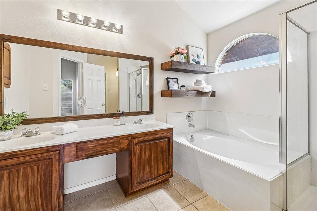 Bathroom featuring a spacious double vanity with wood cabinetry, a large framed mirror, and a built-in bathtub with an arched window