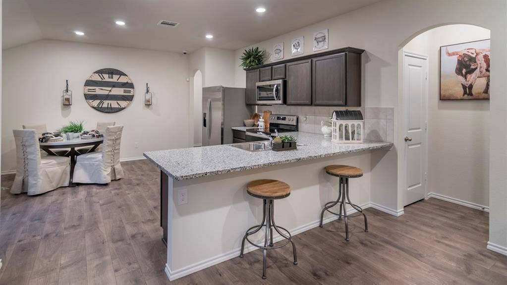 5618 Gannet Place, Crandall, TX 75114 Open-concept interior featuring wood-finish flooring, a kitchen island with stone countertops and a breakfast bar, and dark wood cabinetry with stainless steel appliances