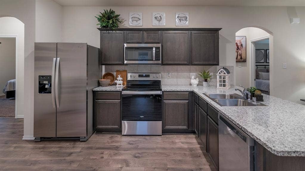 5618 Gannet Place, Crandall, TX 75114 Well-appointed kitchen featuring wood-finish flooring, dark wood cabinetry, stainless steel appliances, and light-toned speckled countertops with a tile backsplash