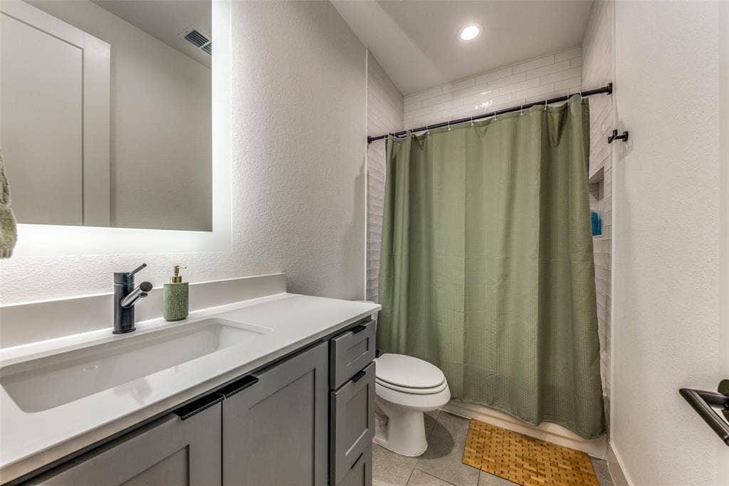 1116 Muncie Avenue, Dallas, TX 75212 Bathroom featuring a white subway tile shower surround with a built-in niche, a toilet, a vanity with a white countertop and an integrated sink, and gray cabinetry with black hardware