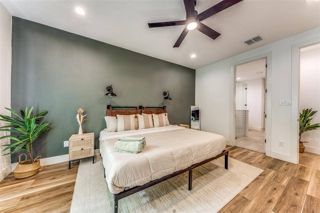 1116 Muncie Avenue, Dallas, TX 75212 Bedroom featuring a dark accent wall, wood-finish flooring, a contemporary ceiling fan with integrated lighting, recessed lighting, and a doorway to a bathroom with tiled walls