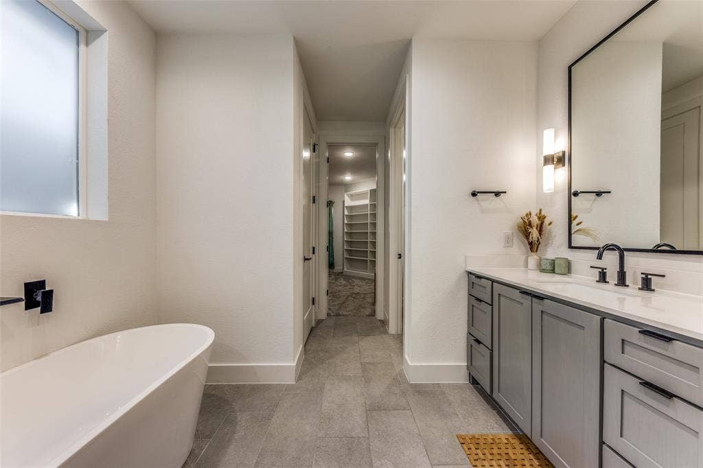 1116 Muncie Avenue, Dallas, TX 75212 Contemporary bathroom featuring a freestanding tub, a vanity with gray cabinetry and matte black hardware, and a large framed mirror