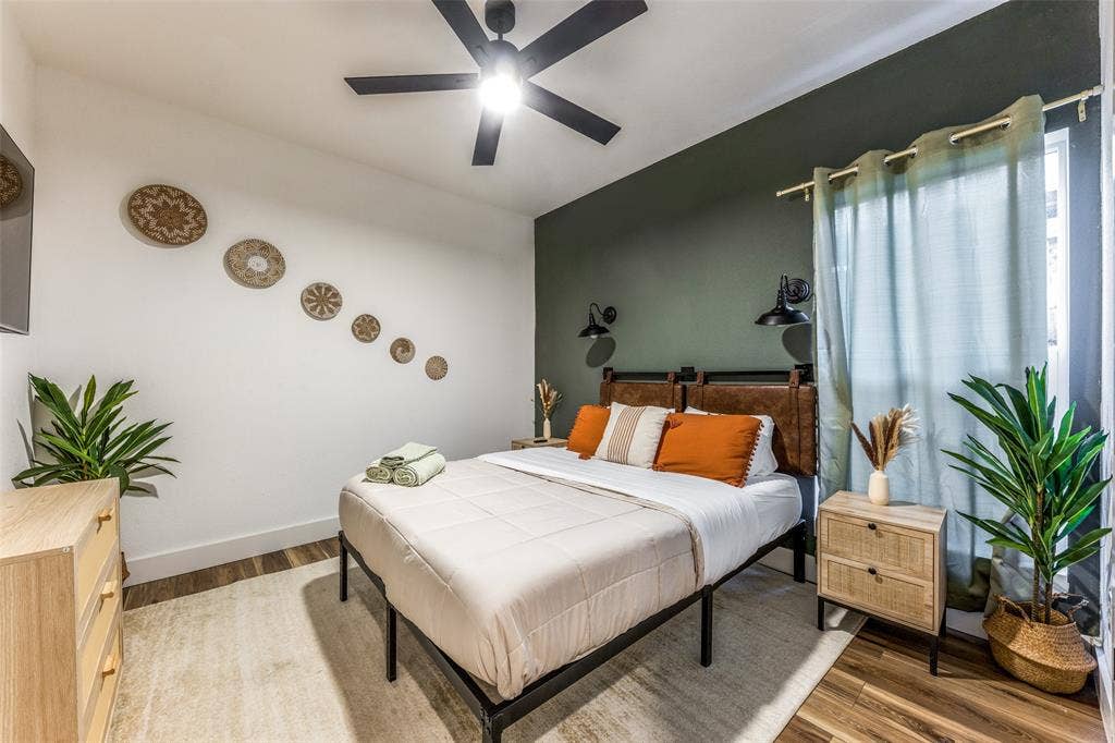 1116 Muncie Avenue, Dallas, TX 75212 Bedroom featuring a dark accent wall, ceiling fan, wood-finish flooring, and a large window with drapes