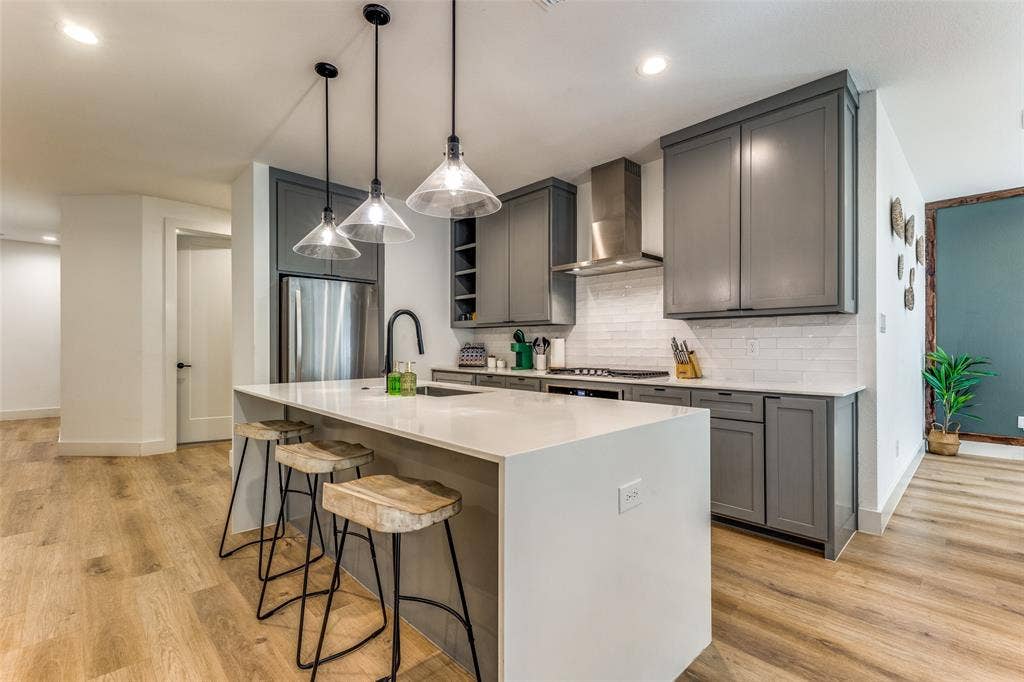 1116 Muncie Avenue, Dallas, TX 75212 Modern kitchen featuring a large island with white countertop, gray cabinetry, stainless steel appliances, a subway tile backsplash, and wood-finish flooring