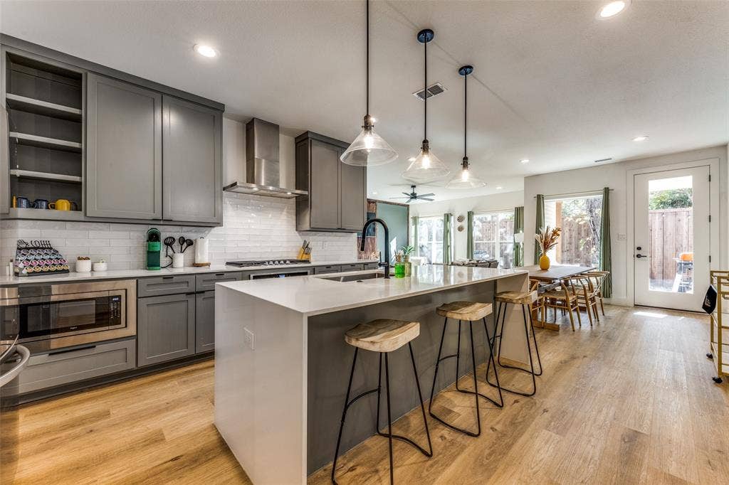 1116 Muncie Avenue, Dallas, TX 75212 Open-concept kitchen featuring an oversized island with seating, pendant lighting, stainless steel appliances, and wood-finish flooring