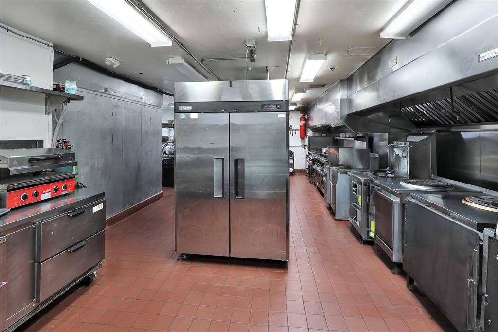 6601 Mediterranean Drive, #6101, McKinney, TX 75072 Commercial kitchen featuring extensive stainless steel appliances, red tile flooring, and overhead fluorescent lighting