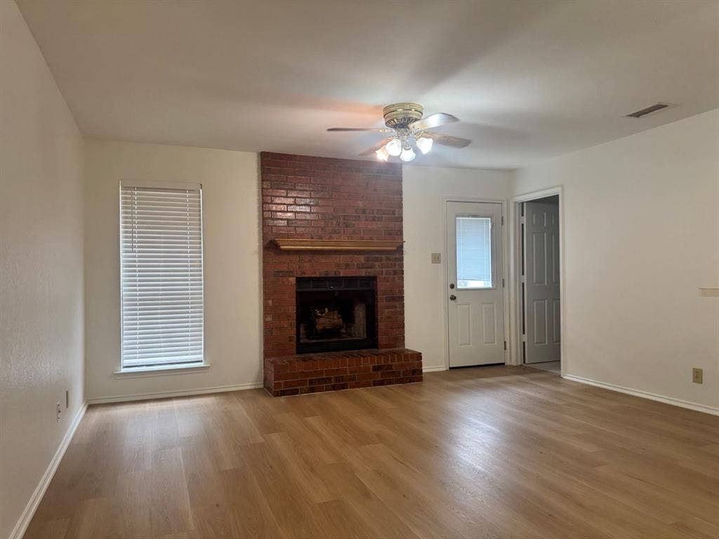 2812 Howard Court, Denton, TX 76209 Spacious room featuring a brick fireplace with a wood mantel, wood-finish flooring, and a ceiling fan with integrated lighting