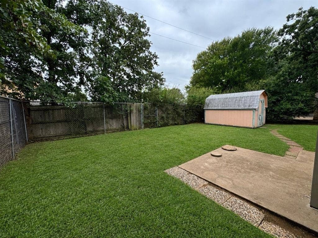 2812 Howard Court, Denton, TX 76209 Expansive grassy yard featuring a detached storage shed, a concrete patio, and a chain-link fence
