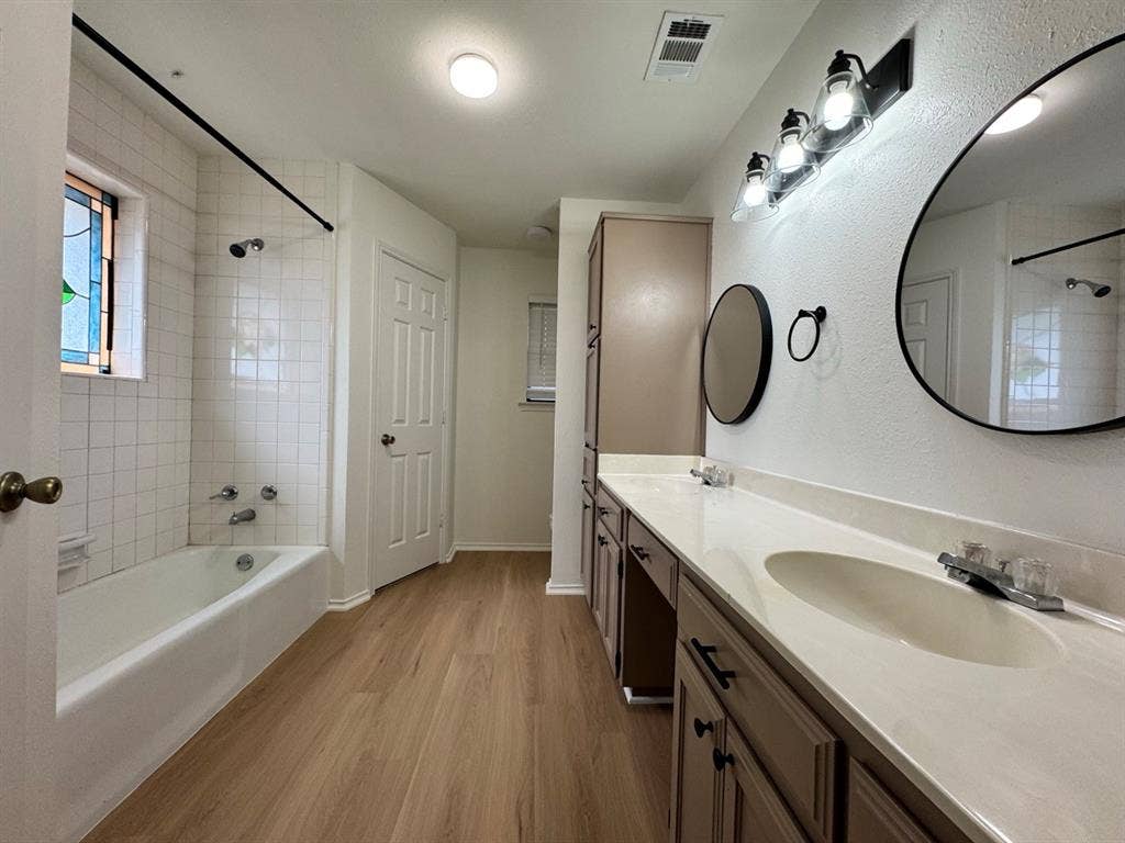 2812 Howard Court, Denton, TX 76209 Bathroom featuring a double vanity with integrated sinks, wood-finish flooring, a white tiled tub/shower combination, and a decorative stained glass window
