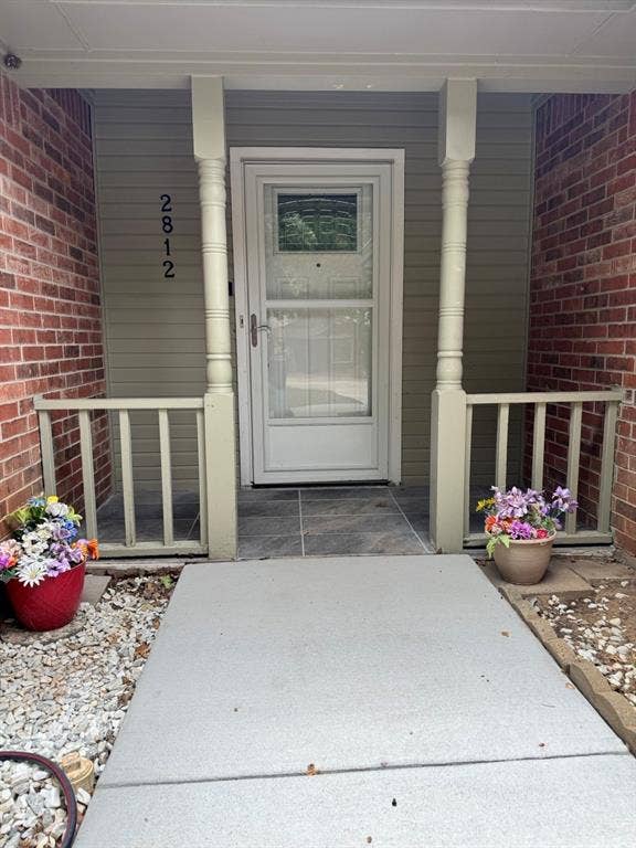 2812 Howard Court, Denton, TX 76209 Covered front porch featuring a white storm door, red brick siding, and decorative turned columns