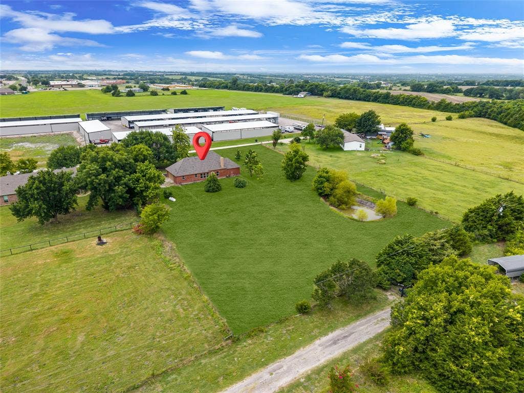 18723 Sims Lane, Nevada, TX 75173 Expansive green acreage featuring a single-story brick residence with a dark shingled roof, surrounding mature trees, and a visible pond