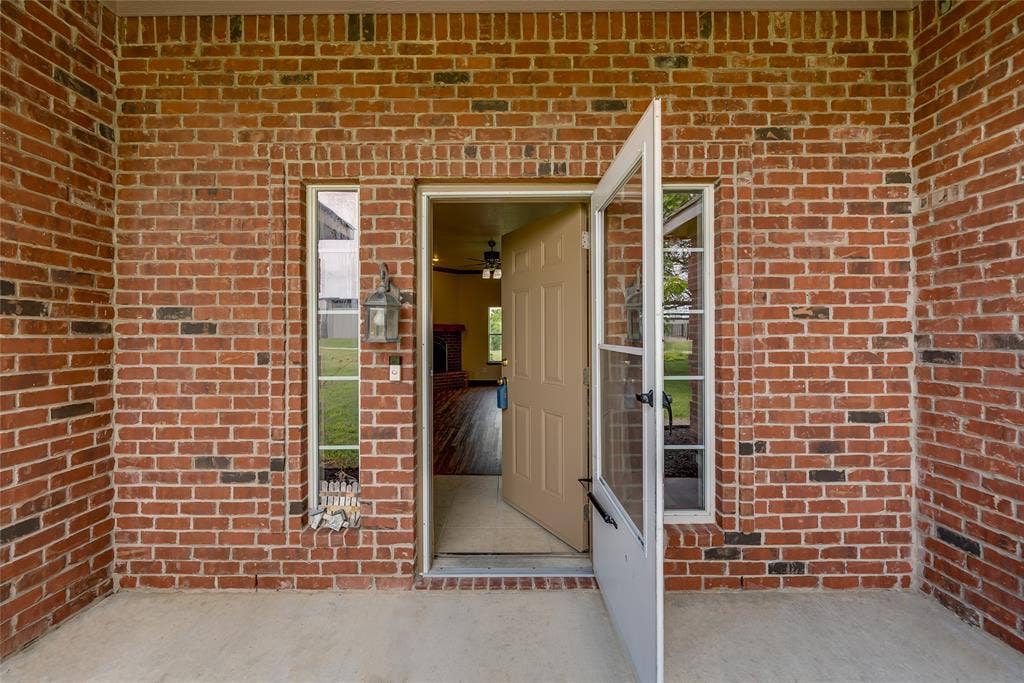 18723 Sims Lane, Nevada, TX 75173 Brick exterior with a covered porch, featuring a tan entry door with a screen door, and vertical window accents