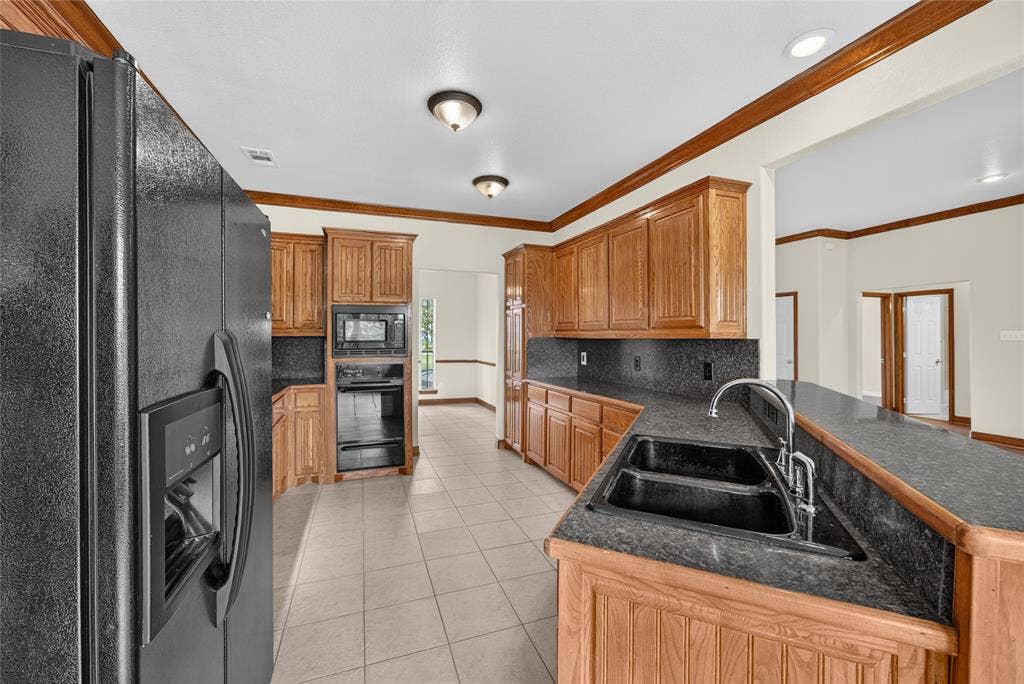 18723 Sims Lane, Nevada, TX 75173 Spacious kitchen featuring extensive wood cabinetry, dark countertops, black double basin sink with chrome faucet, black built-in oven and microwave, and tiled flooring