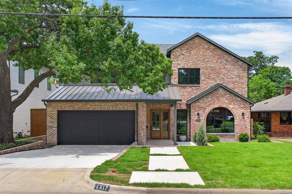 6817 Blessing Drive, Dallas, TX 75214 Contemporary brick exterior with a dark metal roof, a two-car garage with a dark door, a double wood-panel entrance door, and a prominent arched window feature