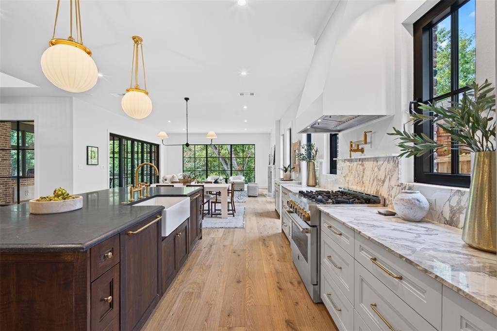 6817 Blessing Drive, Dallas, TX 75214 Gourmet kitchen featuring a substantial island with dark wood cabinetry and a farmhouse sink, light wood-finish flooring, light stone countertops with a full-height backsplash, a professional-grade range, and abundant natural light from numerous windows