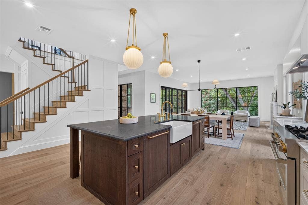 6817 Blessing Drive, Dallas, TX 75214 Open-concept living space featuring a dark wood kitchen island with an integrated farmhouse sink, light wood-finish flooring, and a contemporary staircase with dark iron balusters