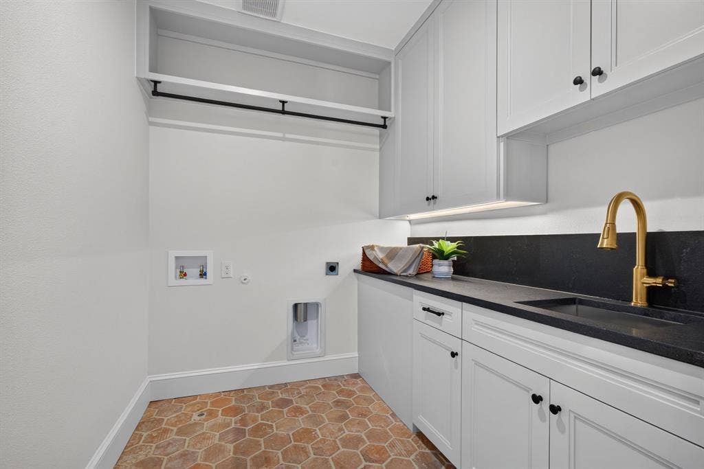6817 Blessing Drive, Dallas, TX 75214 Laundry room featuring hexagonal tile flooring, white shaker cabinetry with black hardware, black countertop with integrated sink, and a brass-finish faucet