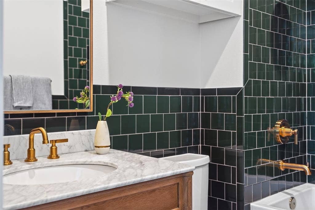 6817 Blessing Drive, Dallas, TX 75214 Bathroom featuring dark green subway tile, a marble-finish countertop, and gold-tone fixtures