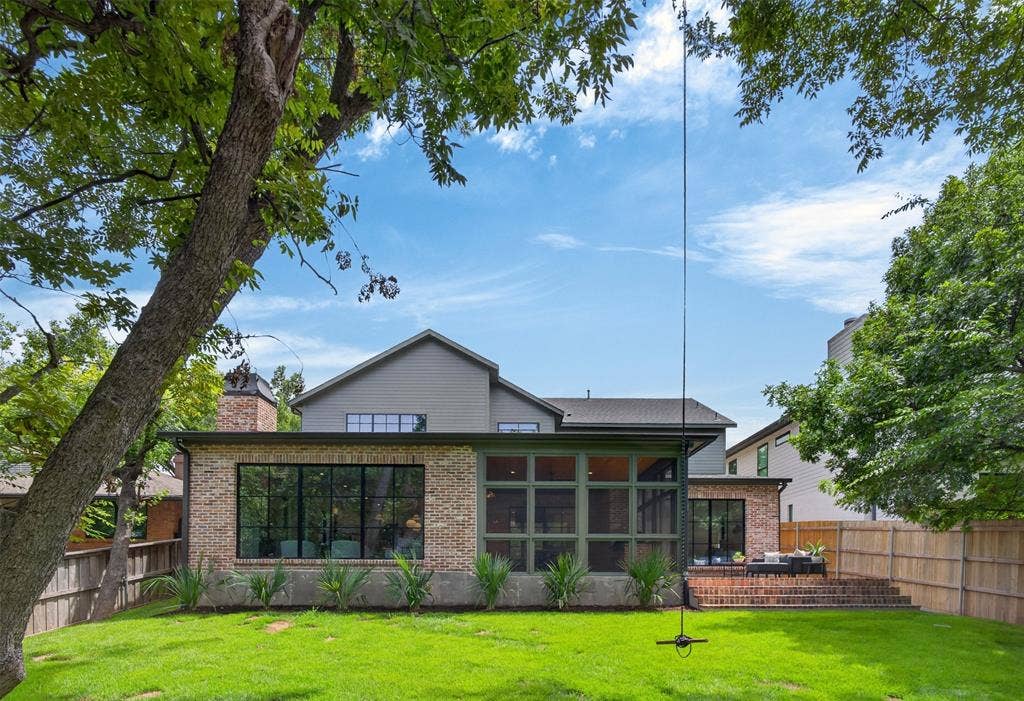 6817 Blessing Drive, Dallas, TX 75214 Expansive rear lawn featuring a brick exterior with large windows, a screened porch, a multi-tiered brick patio, and mature trees providing natural shading