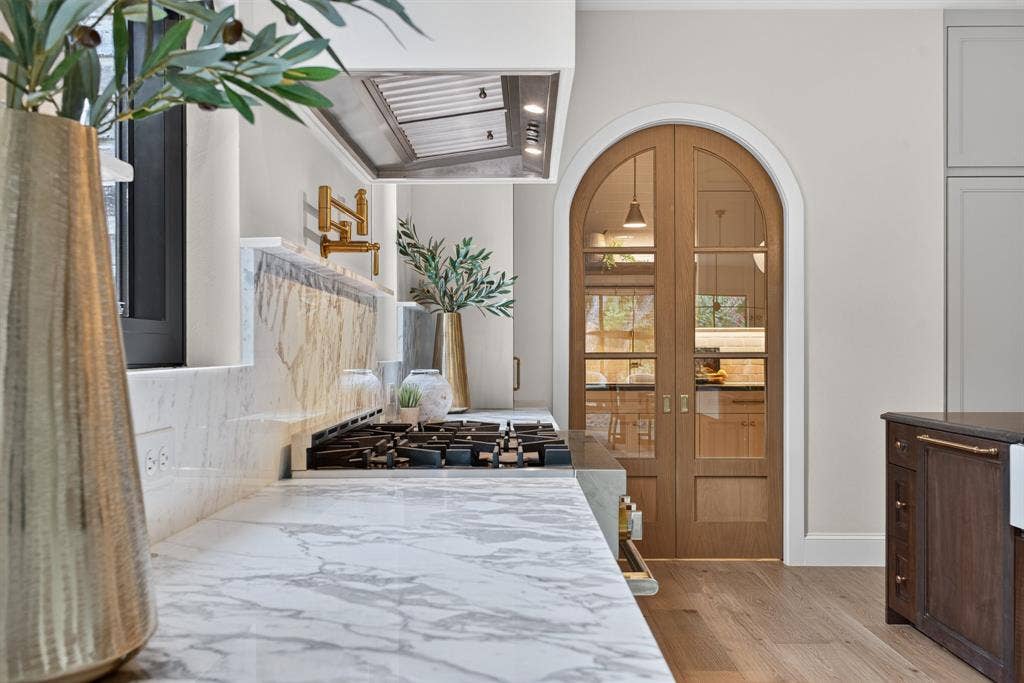 6817 Blessing Drive, Dallas, TX 75214 Gourmet kitchen featuring a built-in gas range, marble countertops and backsplash, a stainless steel range hood, and a gold-tone wall-mounted pot filler