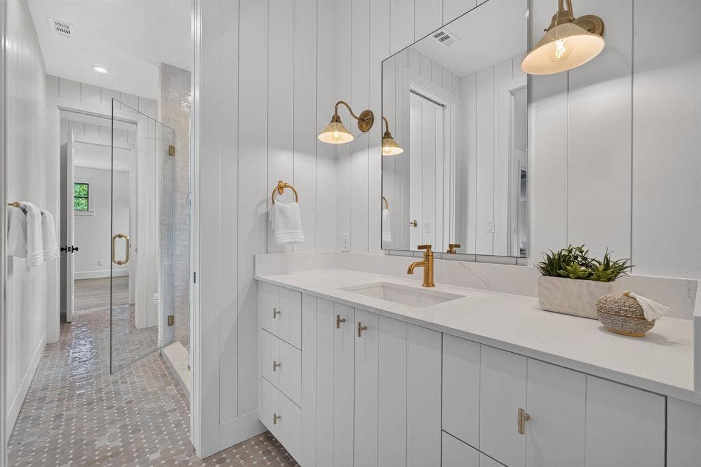 6817 Blessing Drive, Dallas, TX 75214 Bathroom featuring a white vertical shiplap wall, a white vanity with gold hardware, a rectangular undermount sink with a gold faucet, a large frameless mirror, and hexagonal tile flooring