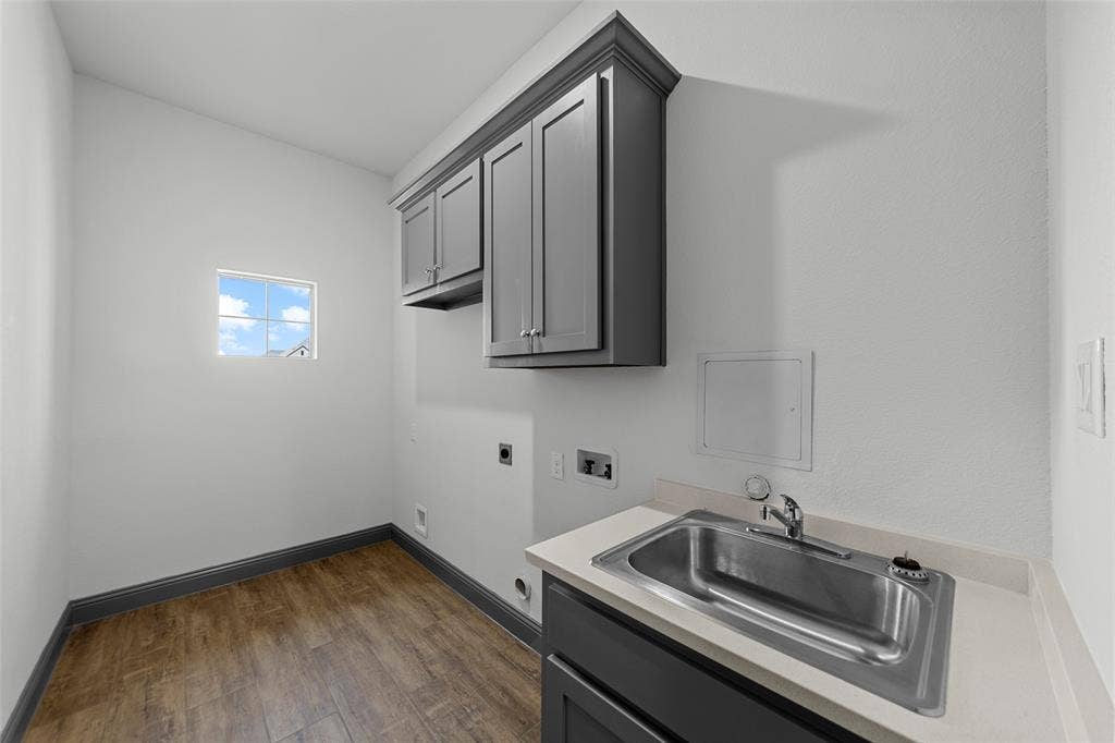 Utility room featuring wood-finish flooring, a wall-mounted window, and built-in cabinetry with a countertop and stainless steel sink