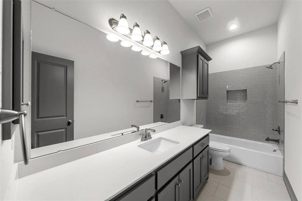 Bathroom featuring a large vanity mirror, an undermount sink, ample counter space, dark wood-finish cabinetry, and a subway tile shower surround with an integrated niche