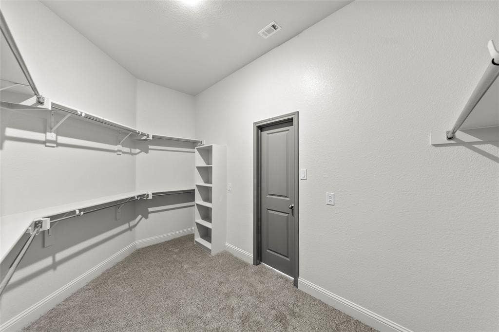 Walk-in closet featuring built-in shelving, hanging rods, an integrated storage tower, light gray carpeting, and white baseboards