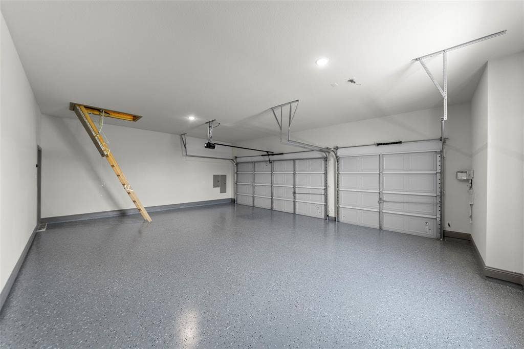Two-car garage featuring a speckled epoxy floor coating, white walls, and a pull-down attic access ladder