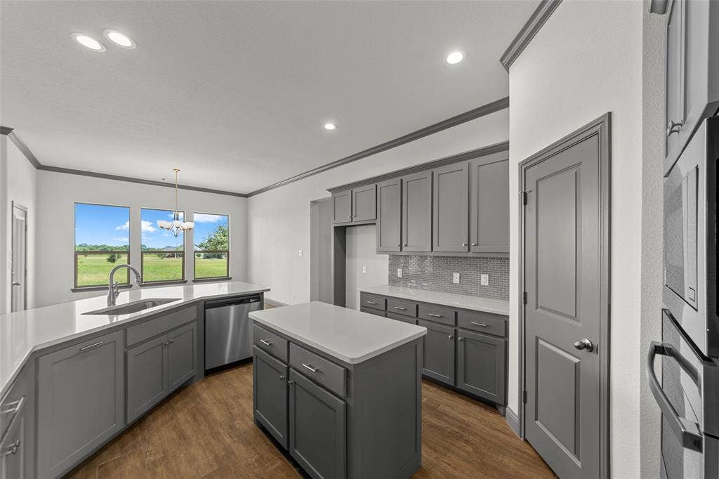 Modern kitchen featuring grey cabinetry, white countertops, stainless steel appliances, and wood-finish flooring