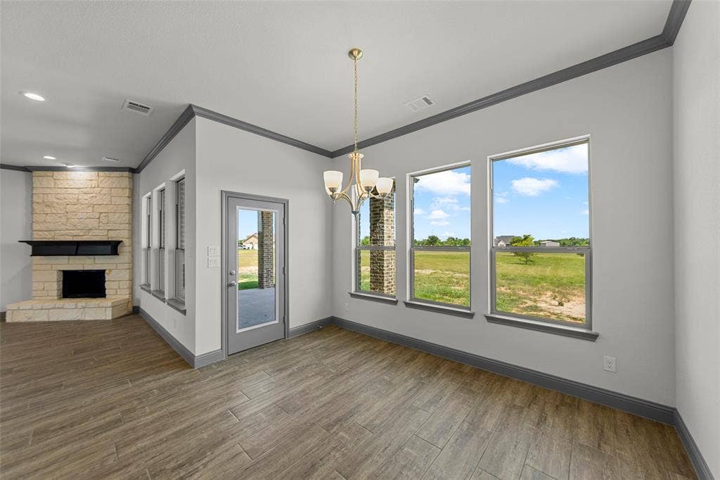 Interior space featuring wood-finish flooring, a stone fireplace with a black mantel, a glass-paneled door, and multiple large windows