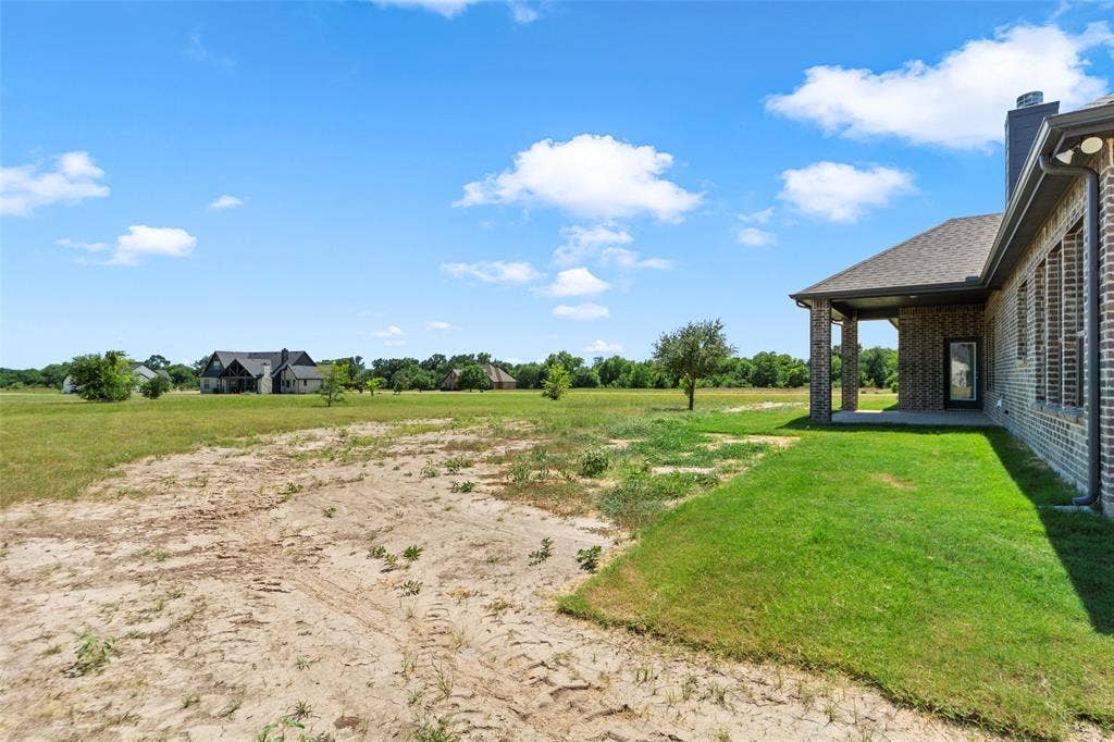 Spacious exterior featuring a covered patio, brick facade, and an expansive grassy area