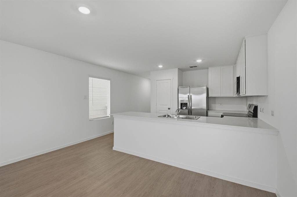6307 Sandpiper Lane, Princeton, TX 75407 Open-concept living space featuring wood-finish flooring, recessed lighting, and a kitchen with stainless steel appliances, white cabinetry, and a peninsula with a sink