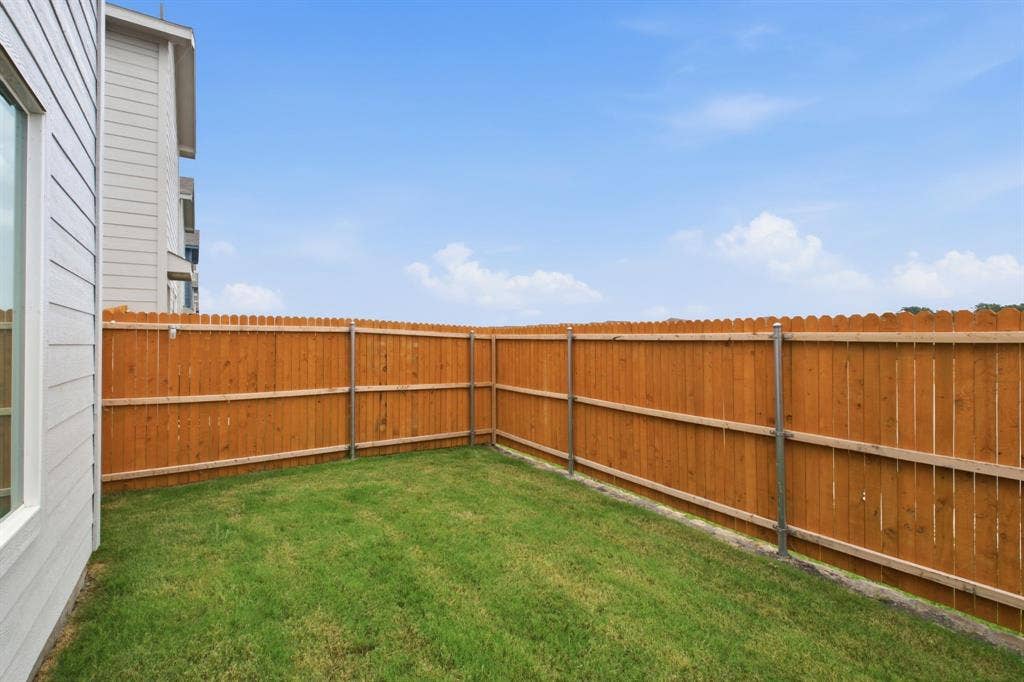 6307 Sandpiper Lane, Princeton, TX 75407 Private backyard space featuring a wood privacy fence, green lawn, and a light-colored exterior wall with a window
