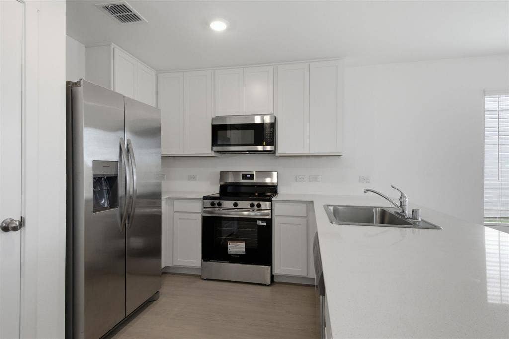 6307 Sandpiper Lane, Princeton, TX 75407 Modern kitchen featuring stainless steel appliances, white cabinetry, a spacious white countertop, an integrated sink, and wood-finish flooring