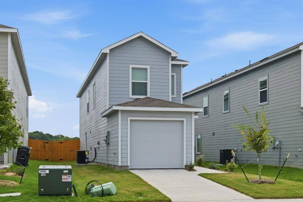 6307 Sandpiper Lane, Princeton, TX 75407 Two-story residence featuring light gray siding, an attached garage, a paved driveway, and a front lawn with a newly planted tree