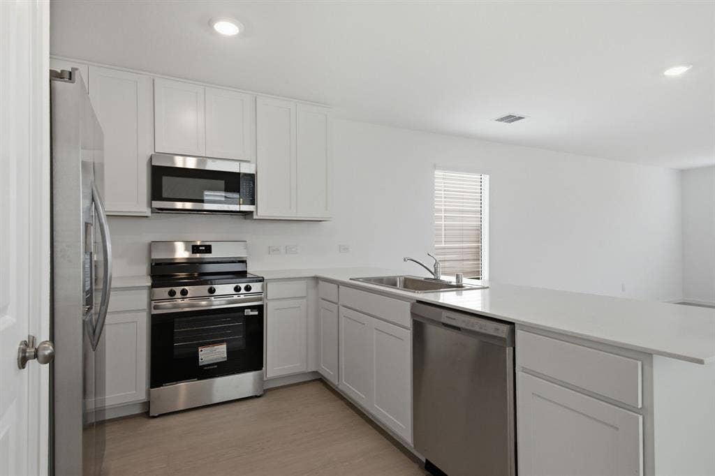 6307 Sandpiper Lane, Princeton, TX 75407 Modern kitchen featuring stainless steel appliances, white cabinetry, integrated sink, light countertops, and wood-finish flooring