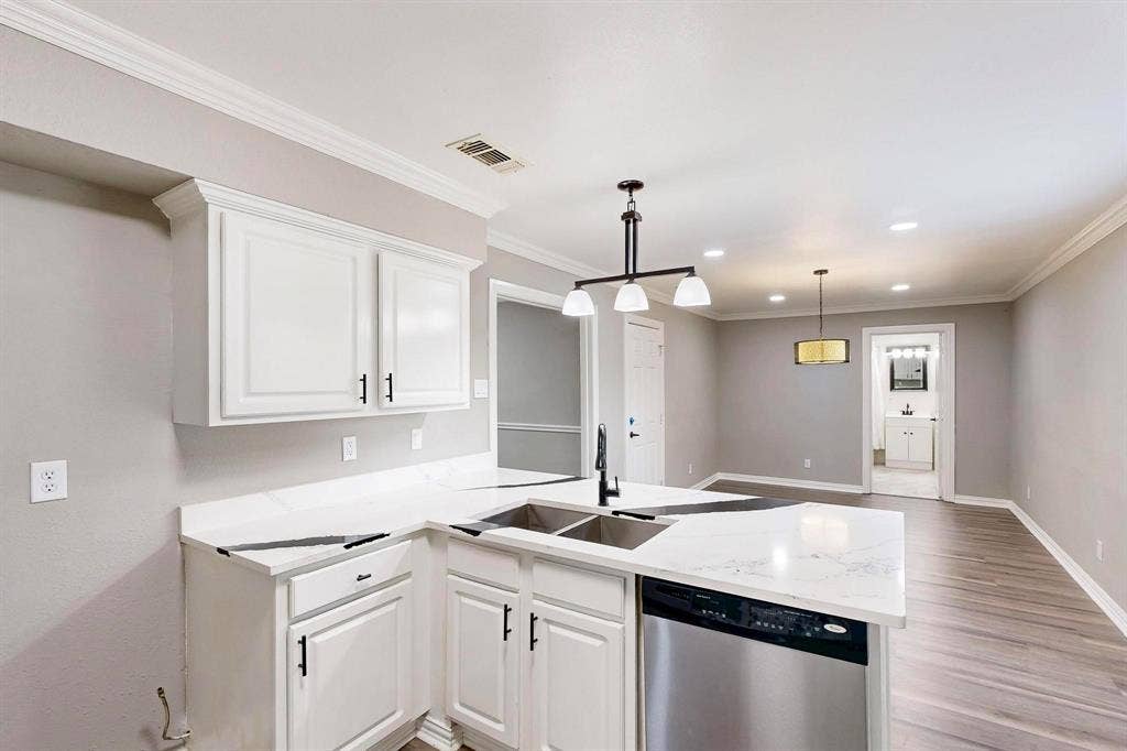 Kitchen featuring stainless steel dishwasher, a sink, a peninsula, baseboards, and white cabinets