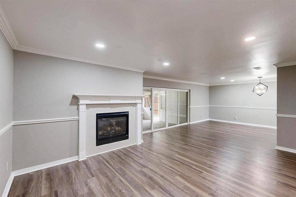Unfurnished living room featuring wood finished floors, a glass covered fireplace, ornamental molding, baseboards, and recessed lighting