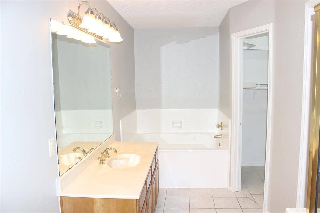 285 Alex Drive, Coppell, TX 75019 Bathroom featuring a wood-finish vanity with a single sink, an integrated bathtub, and tiled flooring