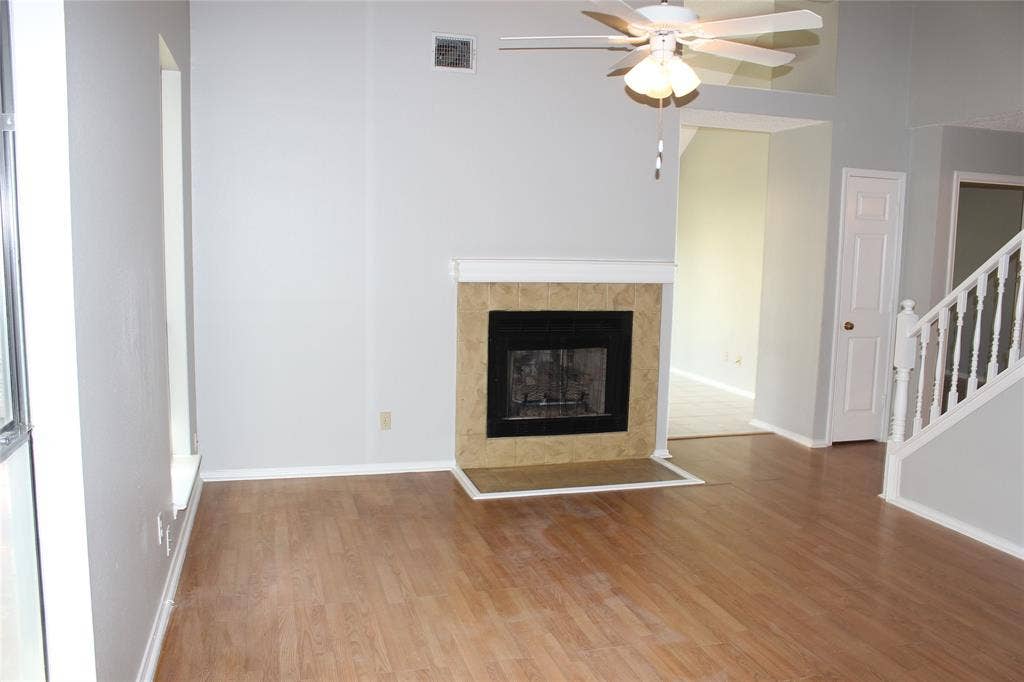 285 Alex Drive, Coppell, TX 75019 Spacious living area featuring a fireplace with a tiled surround, wood-finish flooring, a ceiling fan, and a staircase with a white railing