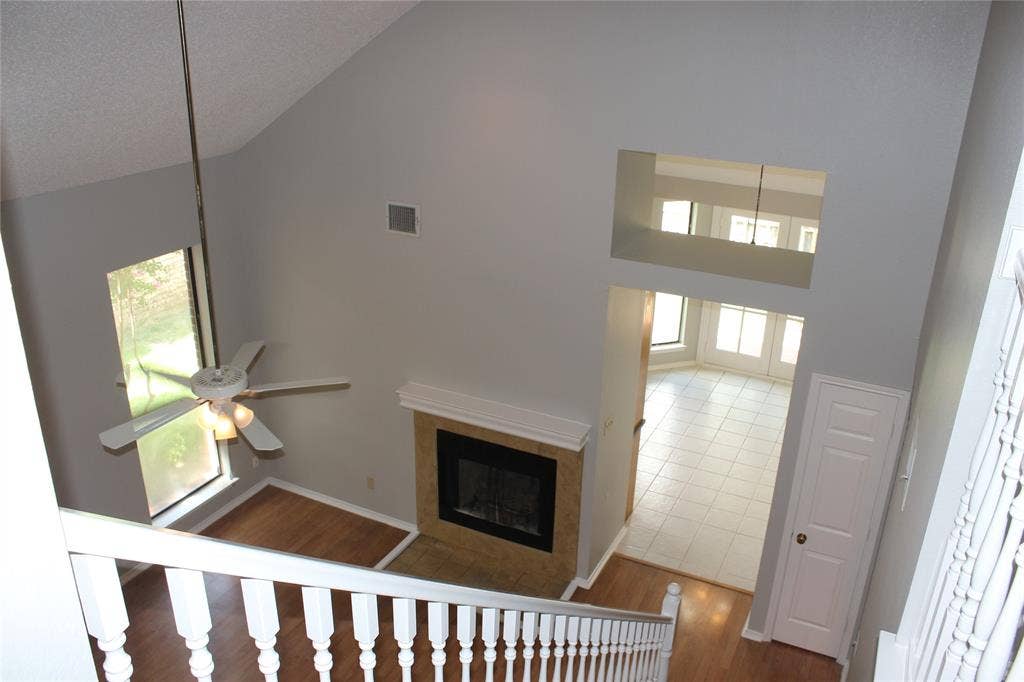 285 Alex Drive, Coppell, TX 75019 Two-story living area with vaulted ceilings and a ceiling fan, featuring a fireplace with a stone surround and mantel
