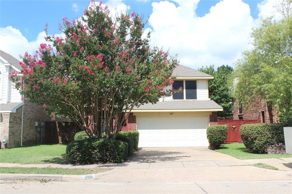 285 Alex Drive, Coppell, TX 75019 Two-story residence featuring a prominent flowering tree, brick facade accents, and light-colored siding
