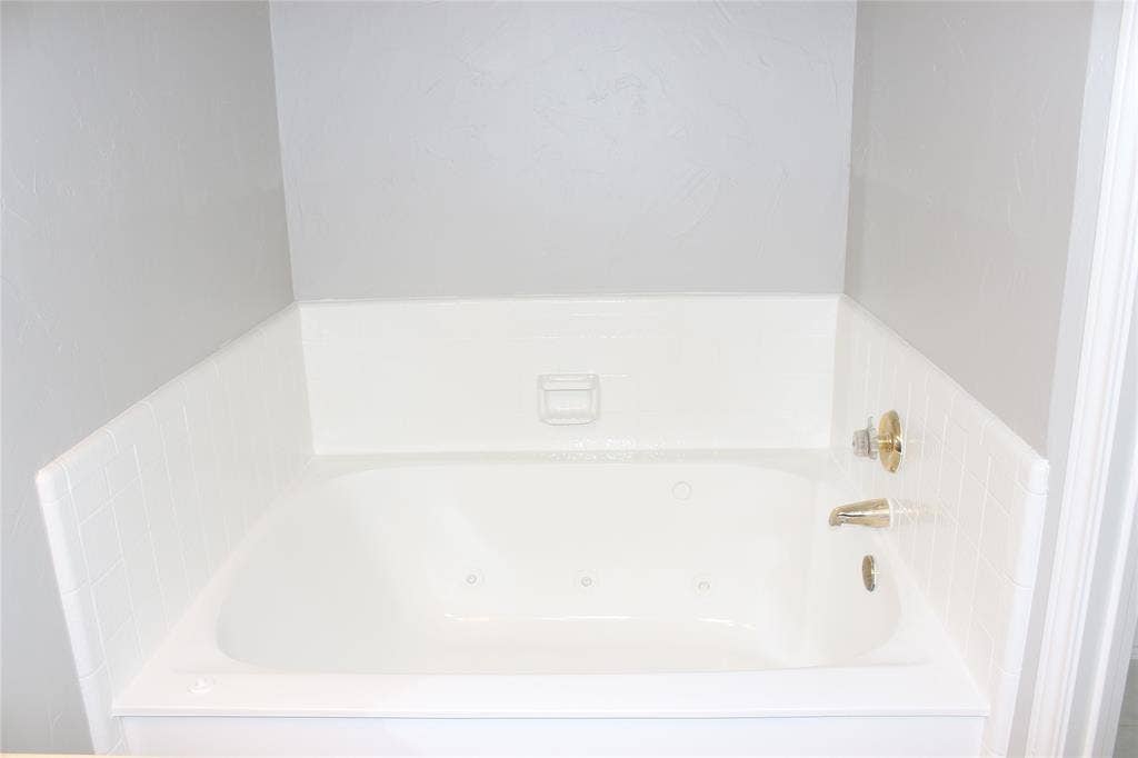285 Alex Drive, Coppell, TX 75019 Soaking tub featuring integrated jets, white tile surround, and polished brass fixtures