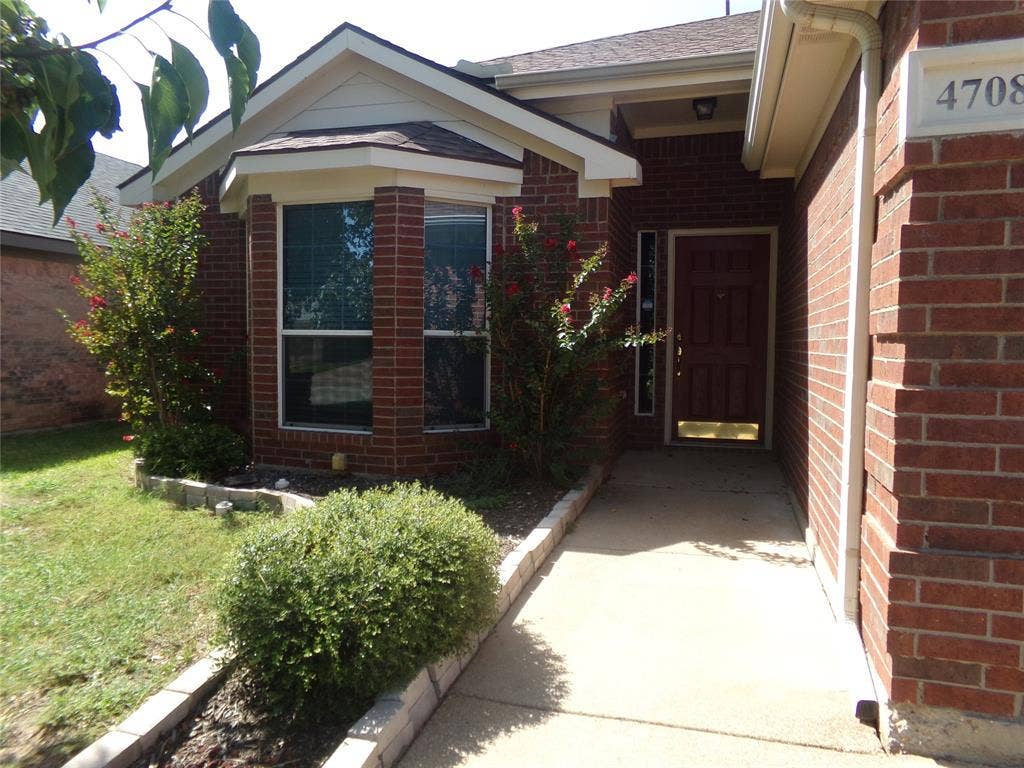 4708 Topaz Lane, Granbury, TX 76049 Brick facade residence featuring a covered entry, a paneled front door with sidelight, and a bay window with blinds