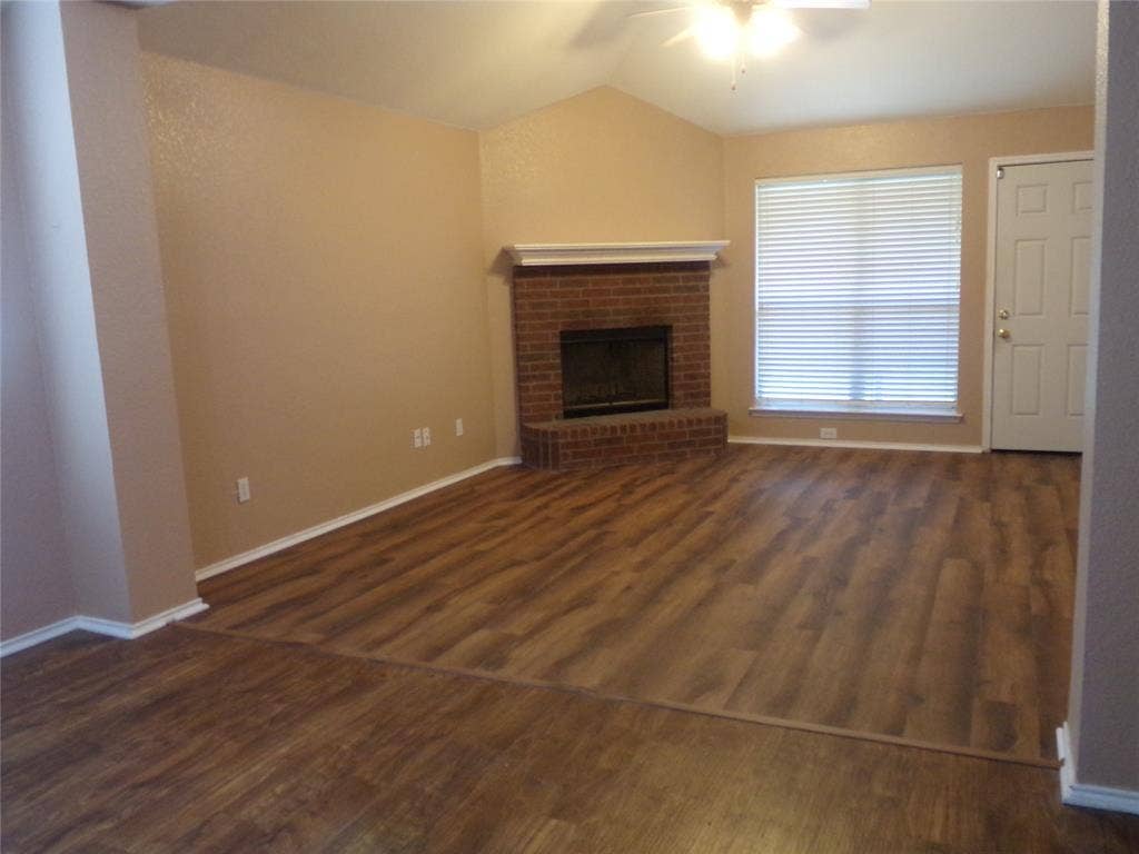 4708 Topaz Lane, Granbury, TX 76049 Living area featuring wood-finish flooring, a brick fireplace with a white mantel, and a vaulted ceiling with a ceiling fan