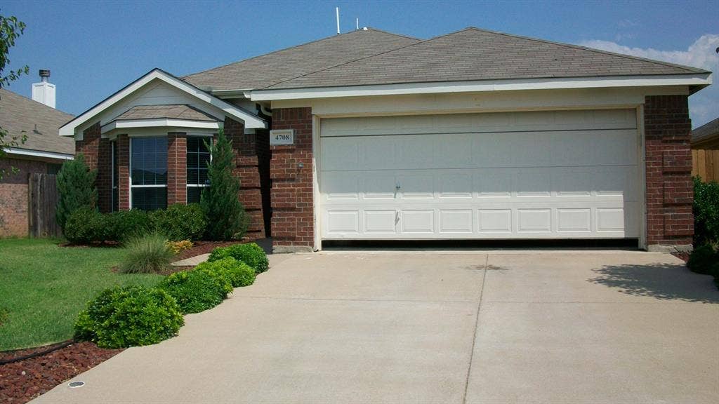 4708 Topaz Lane, Granbury, TX 76049 Brick facade residence featuring a two-car garage, concrete driveway, bay window, and established front landscaping