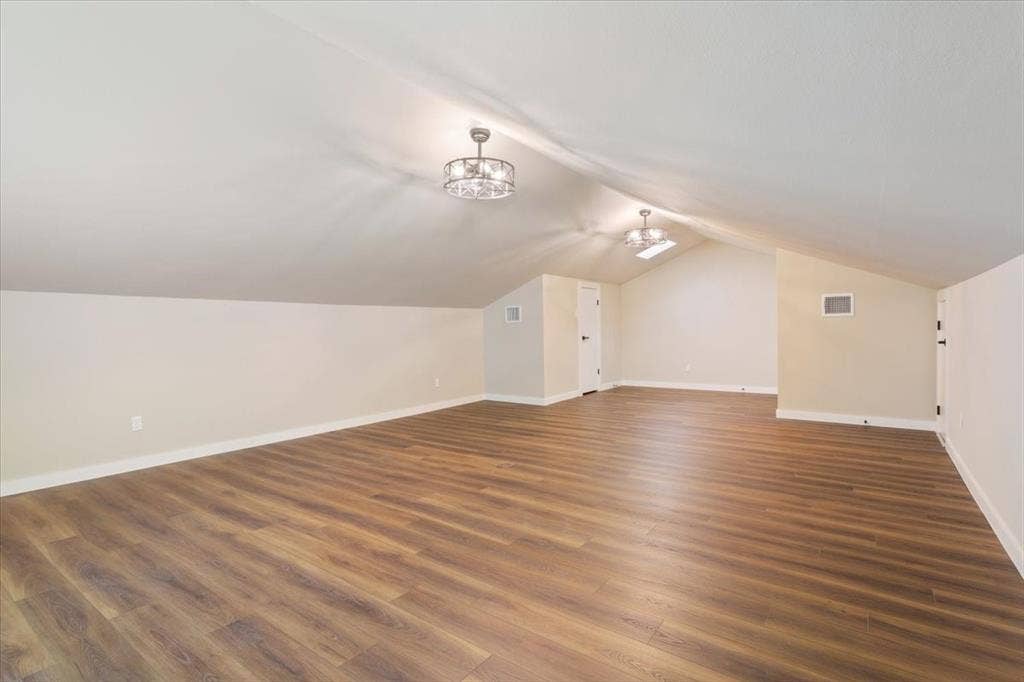 116 Boleman Drive, Hewitt, TX 76643 Spacious 4th bedroom / bonus room featuring LVP wood-finish flooring, a vaulted ceiling, two ceiling-mounted decorative light fixtures with ceiling fans (mini), and attic access